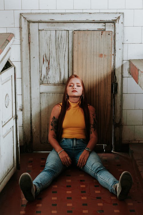 Gratis Wanita Dengan Tank Top Oranye Dan Jeans Denim Biru Duduk Di Lantai Foto Stok