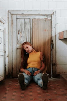 一位年轻女子身着休闲装，轻松地坐在室内的复古木门上，散发着平静的感觉