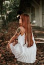 在户外拍摄照片时，一位身穿白色连衣裙的红发女子正在落叶中摆姿势