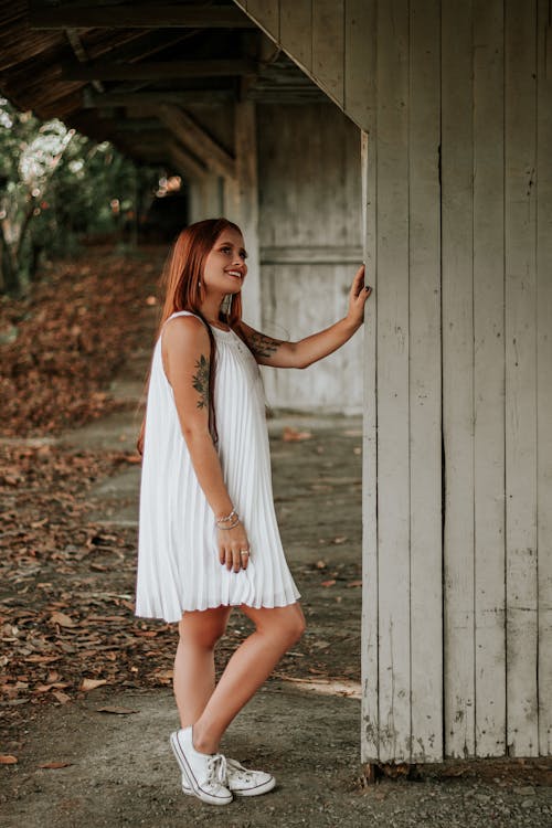 Woman in White Sleeveless Dress Standing Beside Gray Wooden Wall