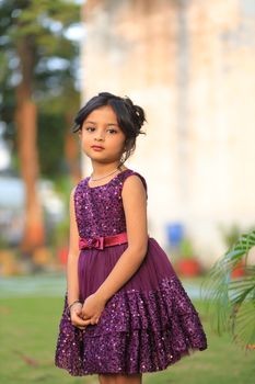 A young girl in a fashionable purple dress poses outdoors, capturing the essence of childhood charm.