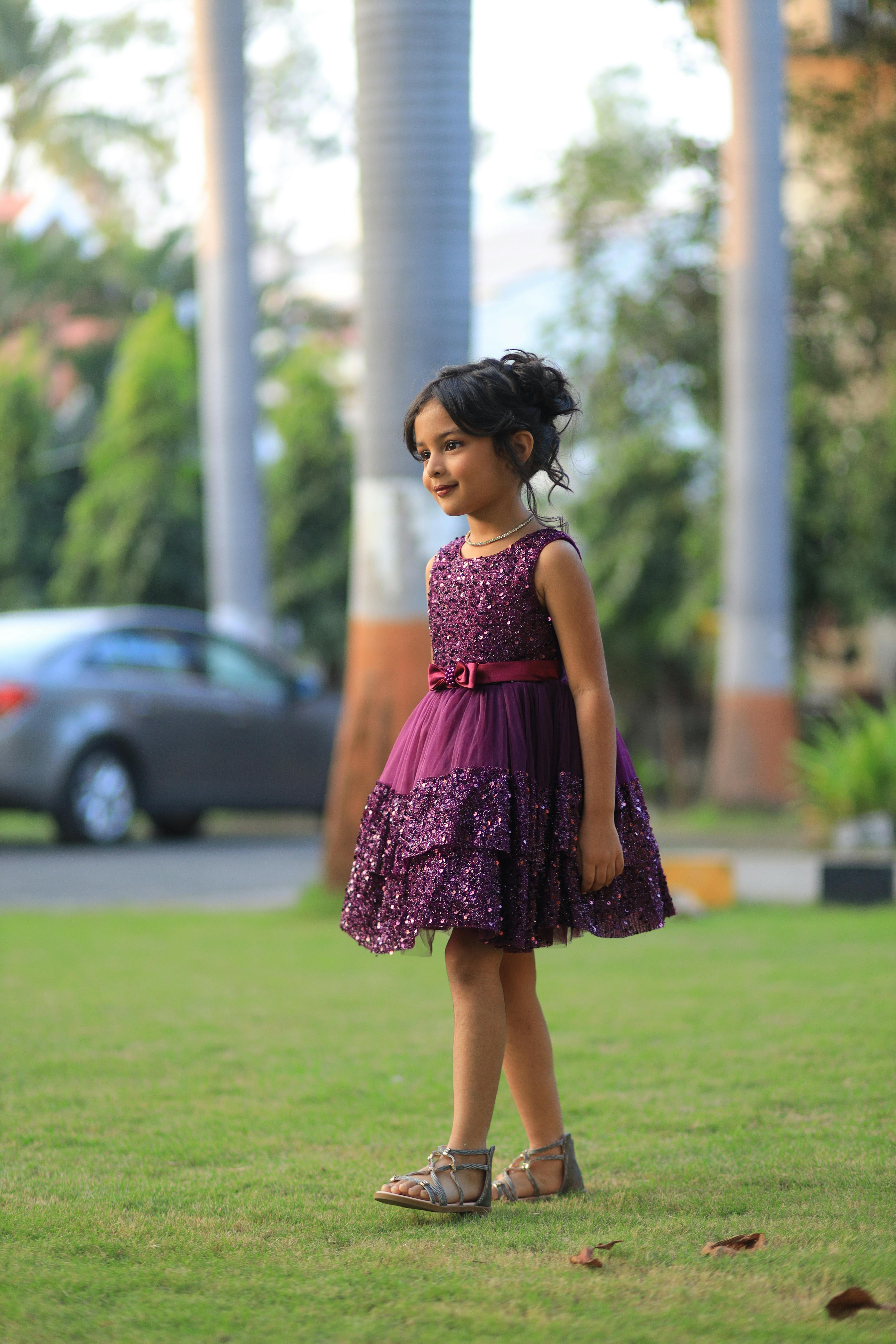 Charming young girl in purple dress walking outdoors, showcasing fashion style.