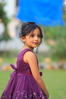 Charming outdoor portrait of a young girl in a stylish purple dress, evoking warmth and style.