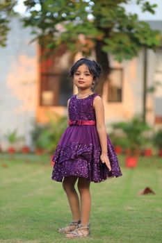 Charming outdoor photoshoot featuring a young girl in a stylish purple dress.