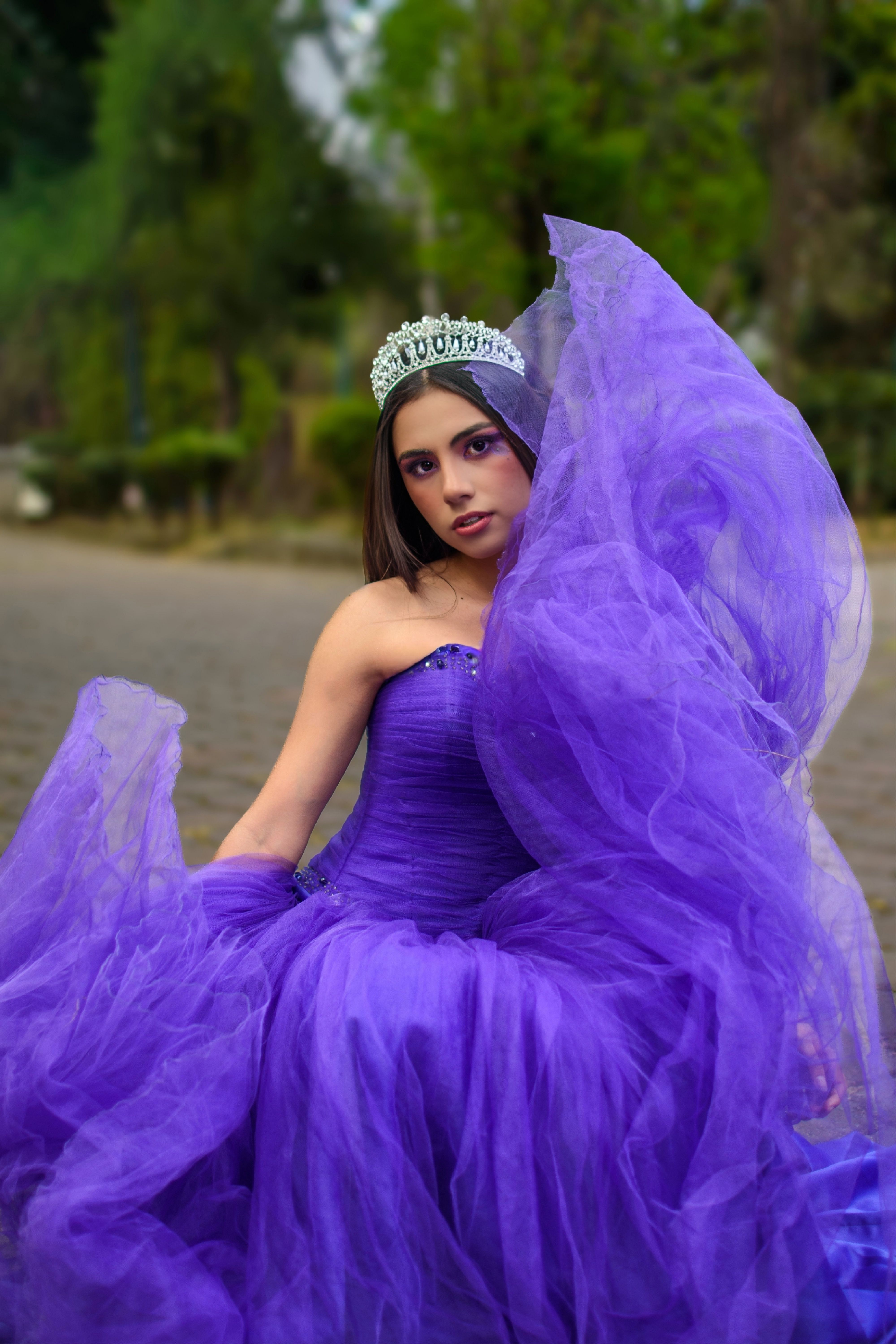 A woman in a flowing purple gown with tiara sits outdoors in Ciudad de México.