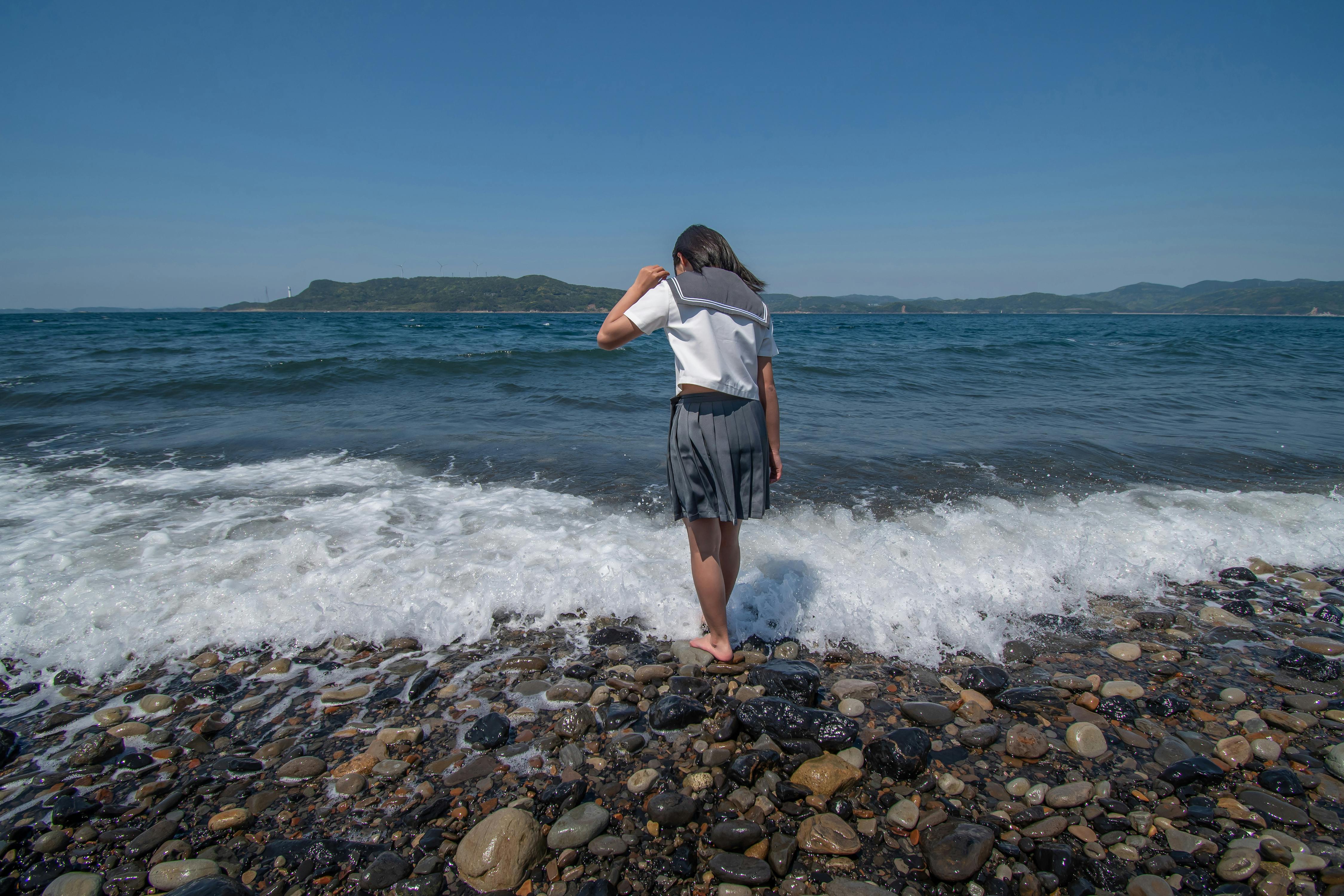 Young girl touching the waves on a pebble beach in Nagasaki, Japan.