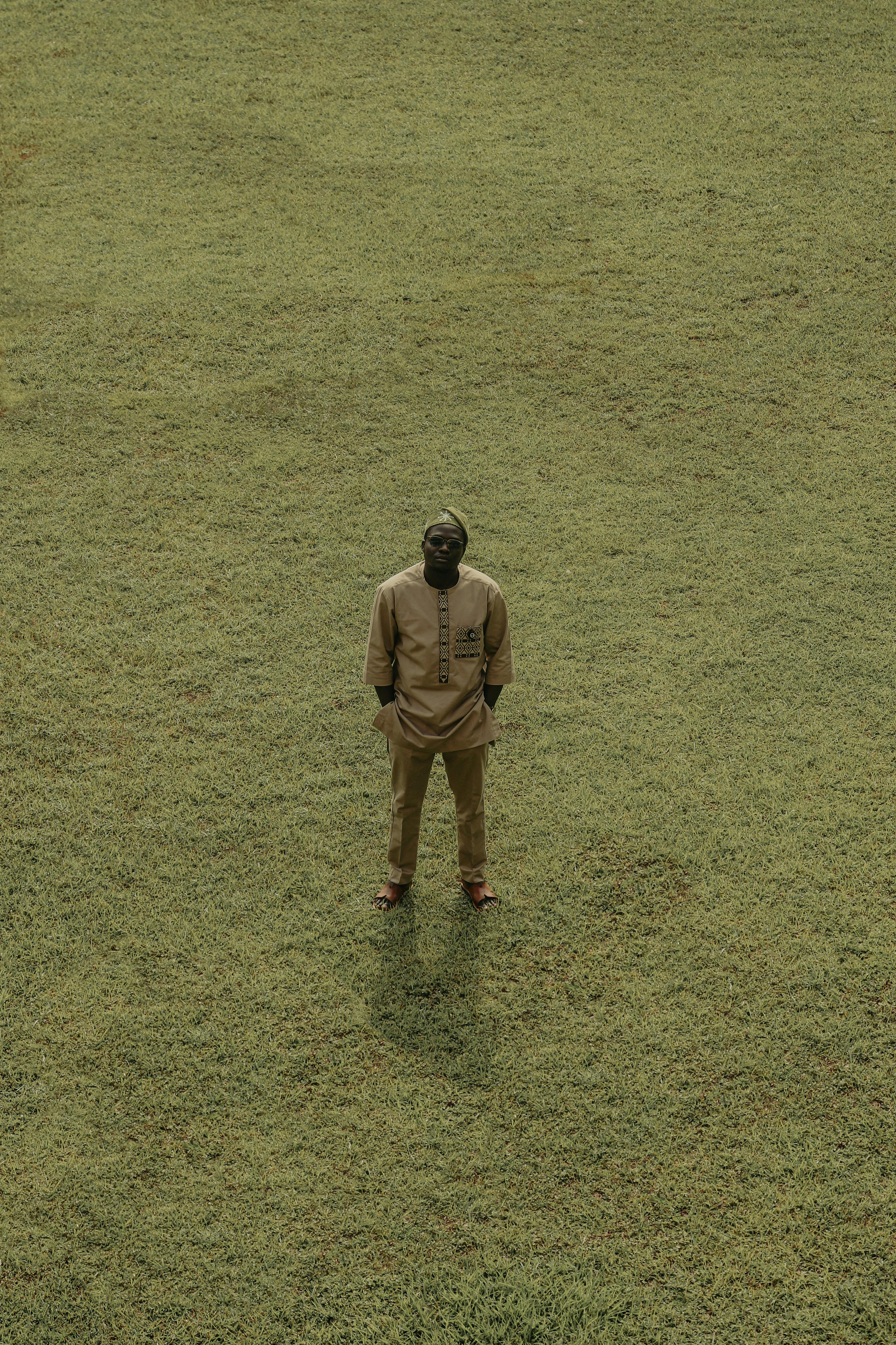 Aerial shot of a person in traditional attire standing on a grassy field, creating a minimalist and serene scene.