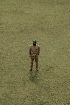Aerial shot of a person in traditional attire standing on a grassy field, creating a minimalist and serene scene.
