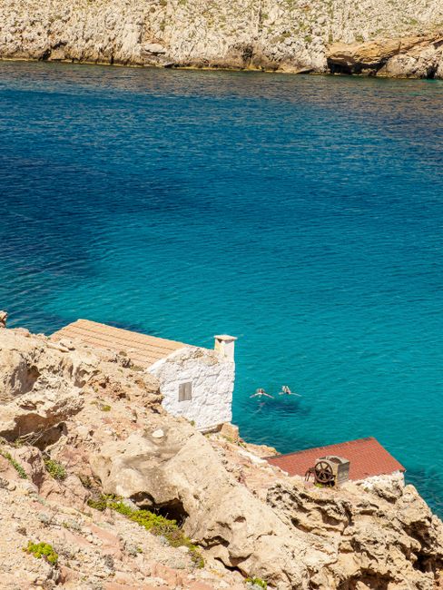 A scenic view of swimmers in crystal-clear water by a rocky cliffside.