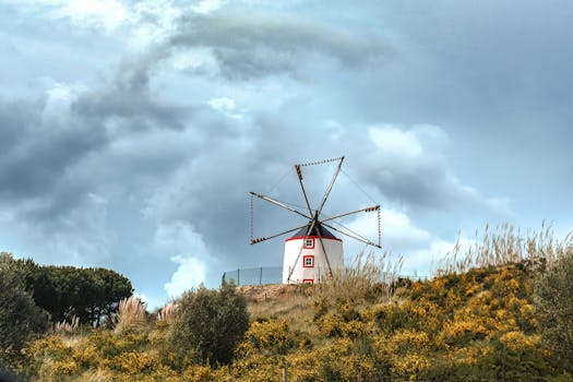 Scenic view of a traditional windmill on a hill in Portugal under a cloudy sky.