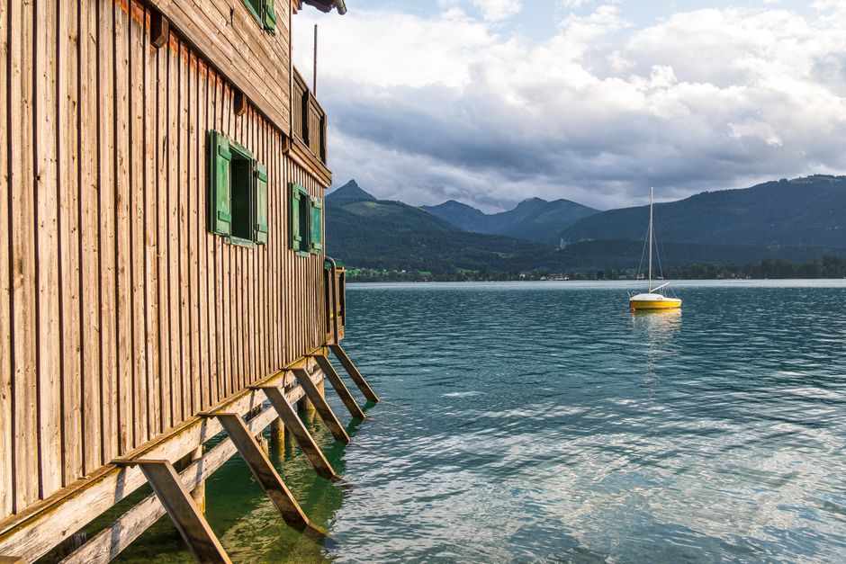 Charming lake view in Austria with wooden boat house and yellow sailboat.