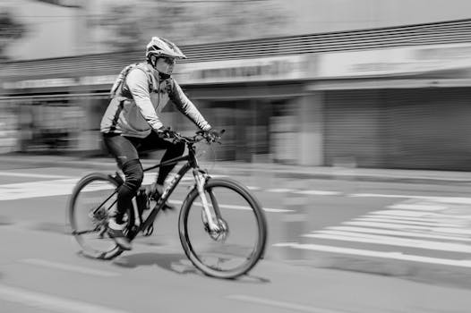 Dynamic black and white image of a cyclist riding through a city street, capturing movement and urban life.