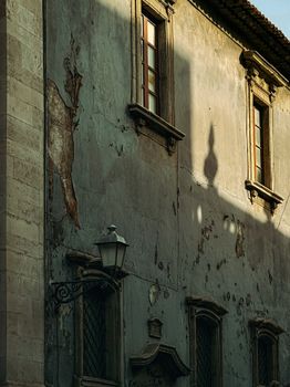 Textured facade of an old Sicilian building with window shadows at sunset.