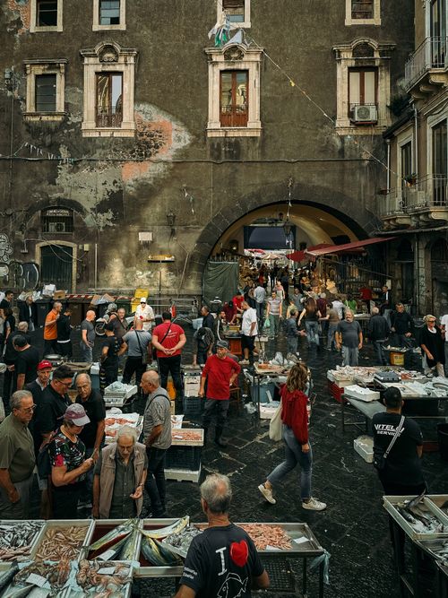 Free Bustling outdoor fish market in Catania, Sicily with locals shopping and socializing under historic architecture. Stock Photo