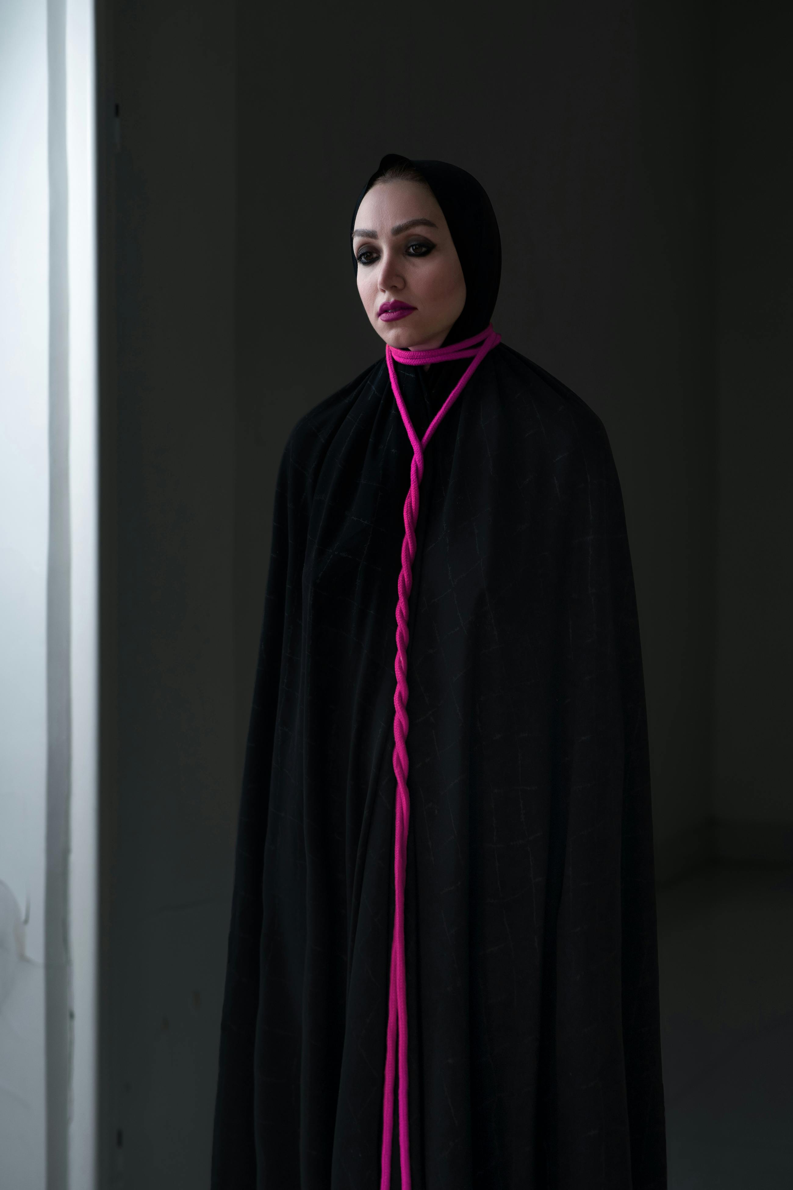 Free Dramatic portrait of a woman in a black cloak with a striking pink accessory. Stock Photo