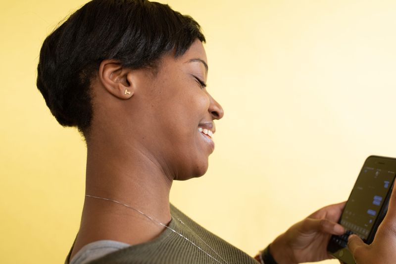 A cheerful woman with short hair texting on her smartphone against a yellow background