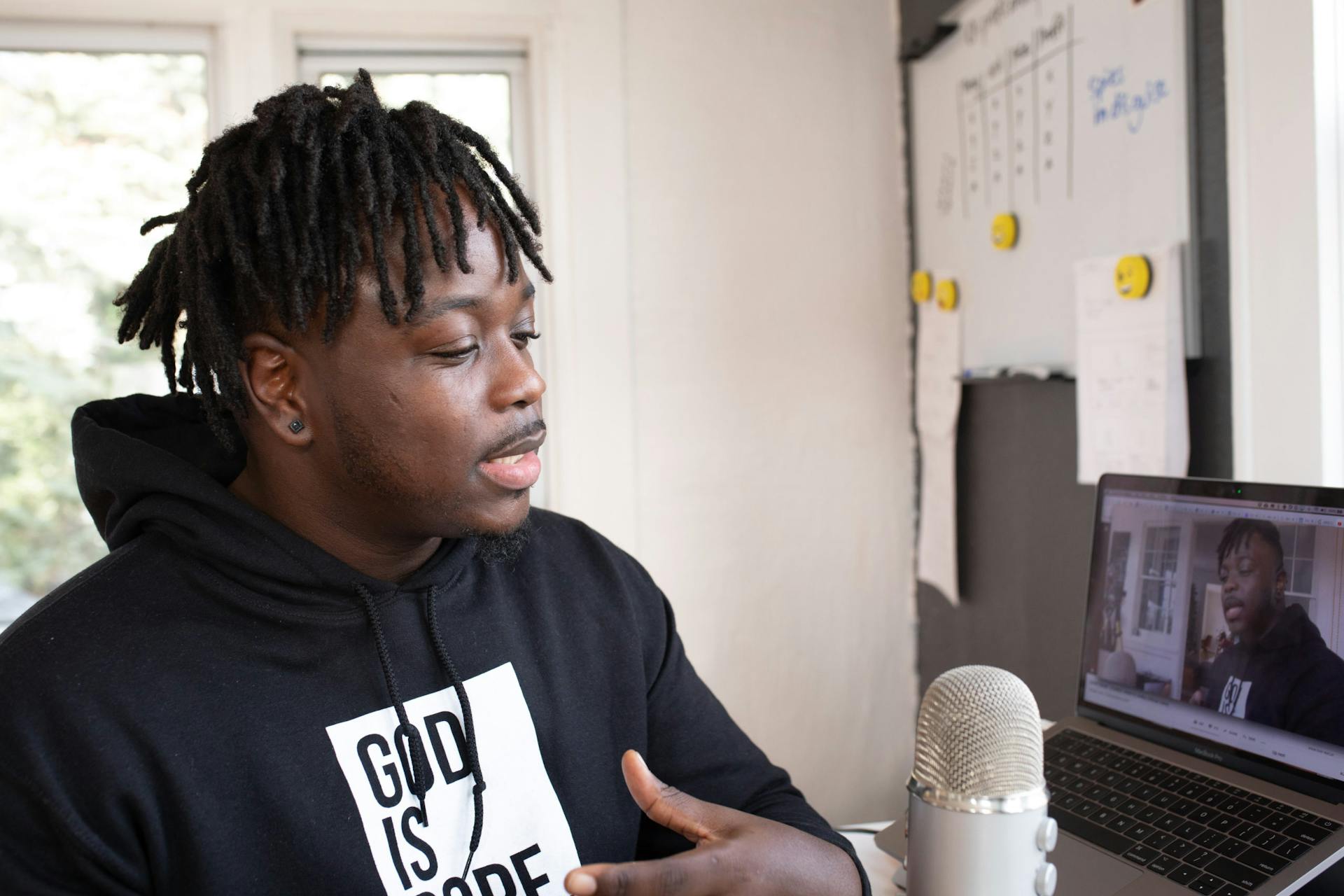 Man recording a podcast indoors with a laptop and microphone, focused and speaking.