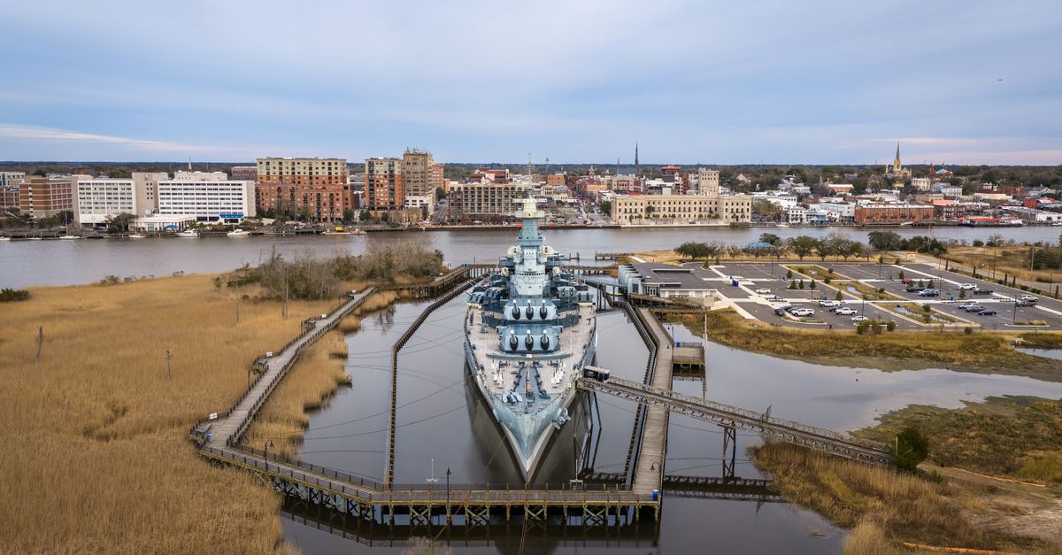 Stunning aerial shot of the Battleship North Carolina anchored in Wilmington with city skyline in the background.