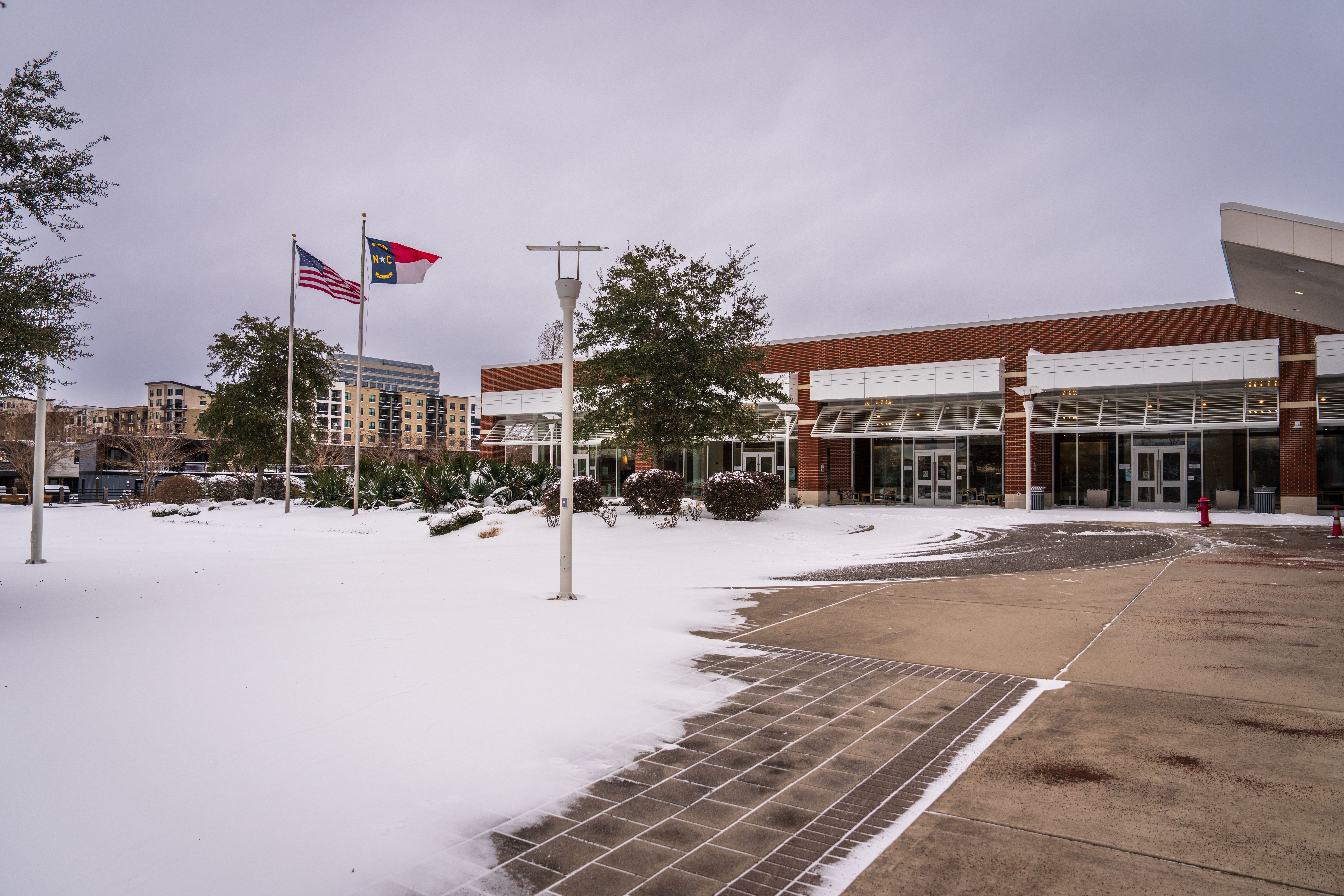 Snow-covered scene outside a North Carolina building with flags and trees.