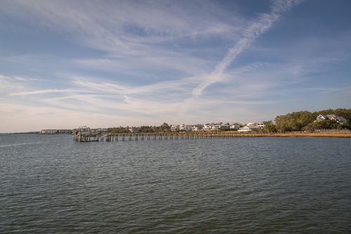 Free A tranquil coastal scene featuring a long wooden pier and waterfront houses under a clear blue sky. Stock Photo
