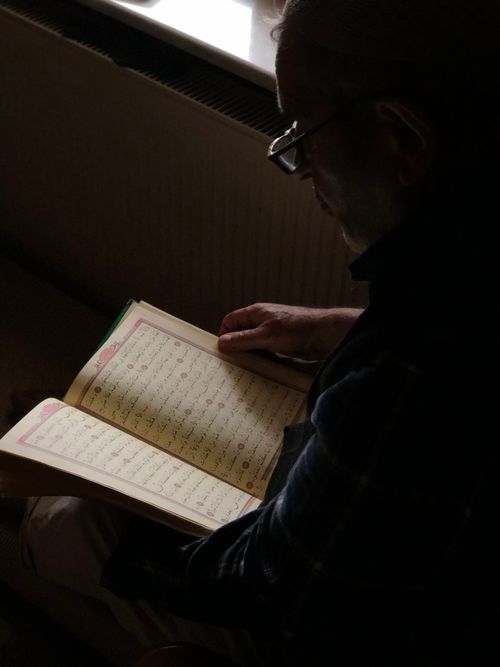 Free A senior man reads a religious book in dim natural light, creating a serene and contemplative atmosphere. Stock Photo