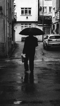 Black and white photo of a person with an umbrella walking through a narrow alleyway on a rainy day.