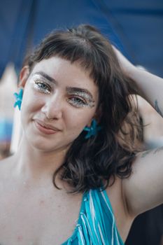 Portrait of a woman with glitter makeup wearing a blue dress, shot outdoors in daylight.