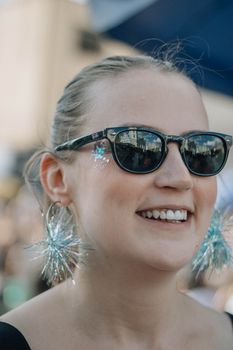 Smiling woman wearing sunglasses and bright earrings at an outdoor event, capturing a festive mood.