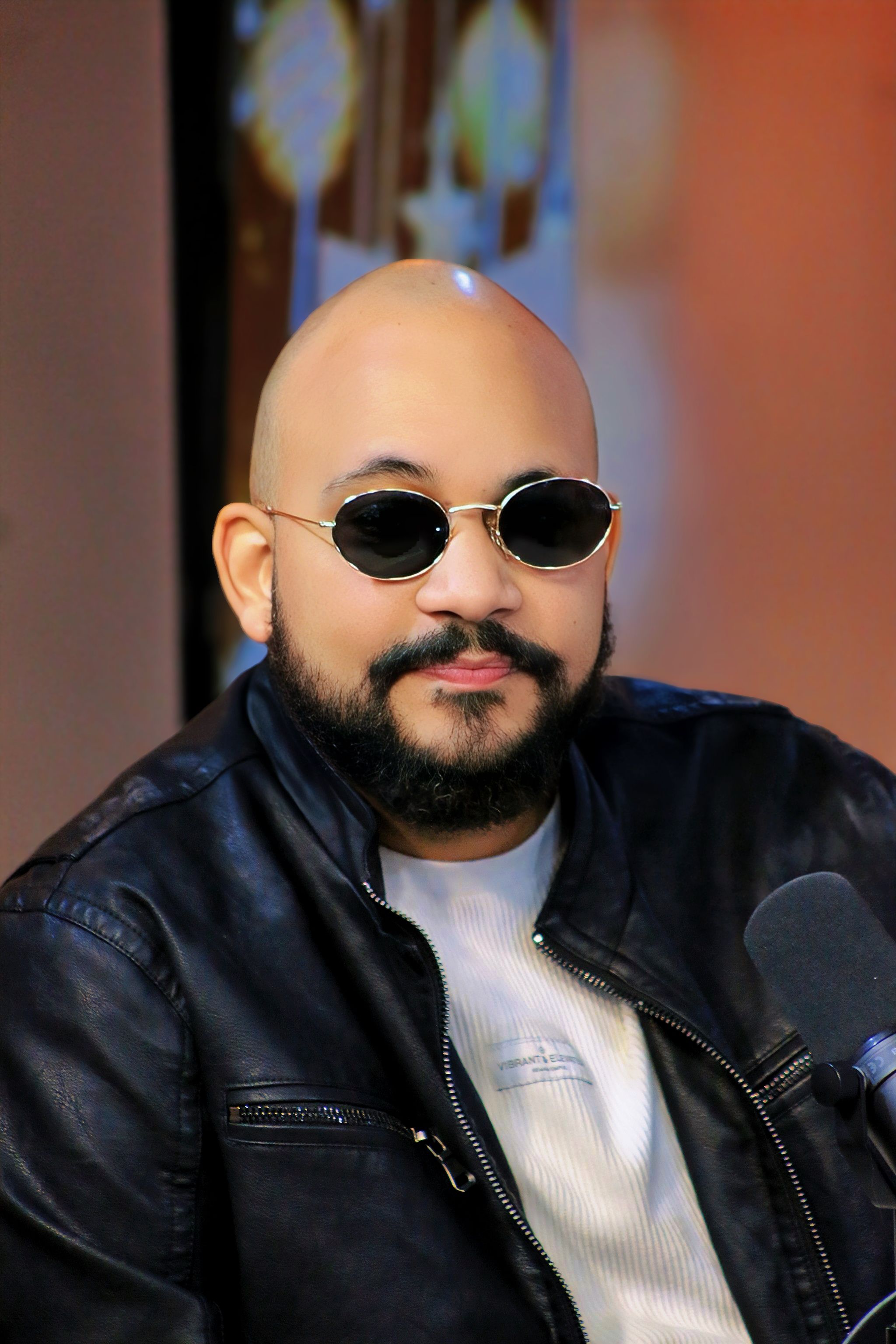 Portrait of a stylish man in sunglasses and leather jacket indoors.