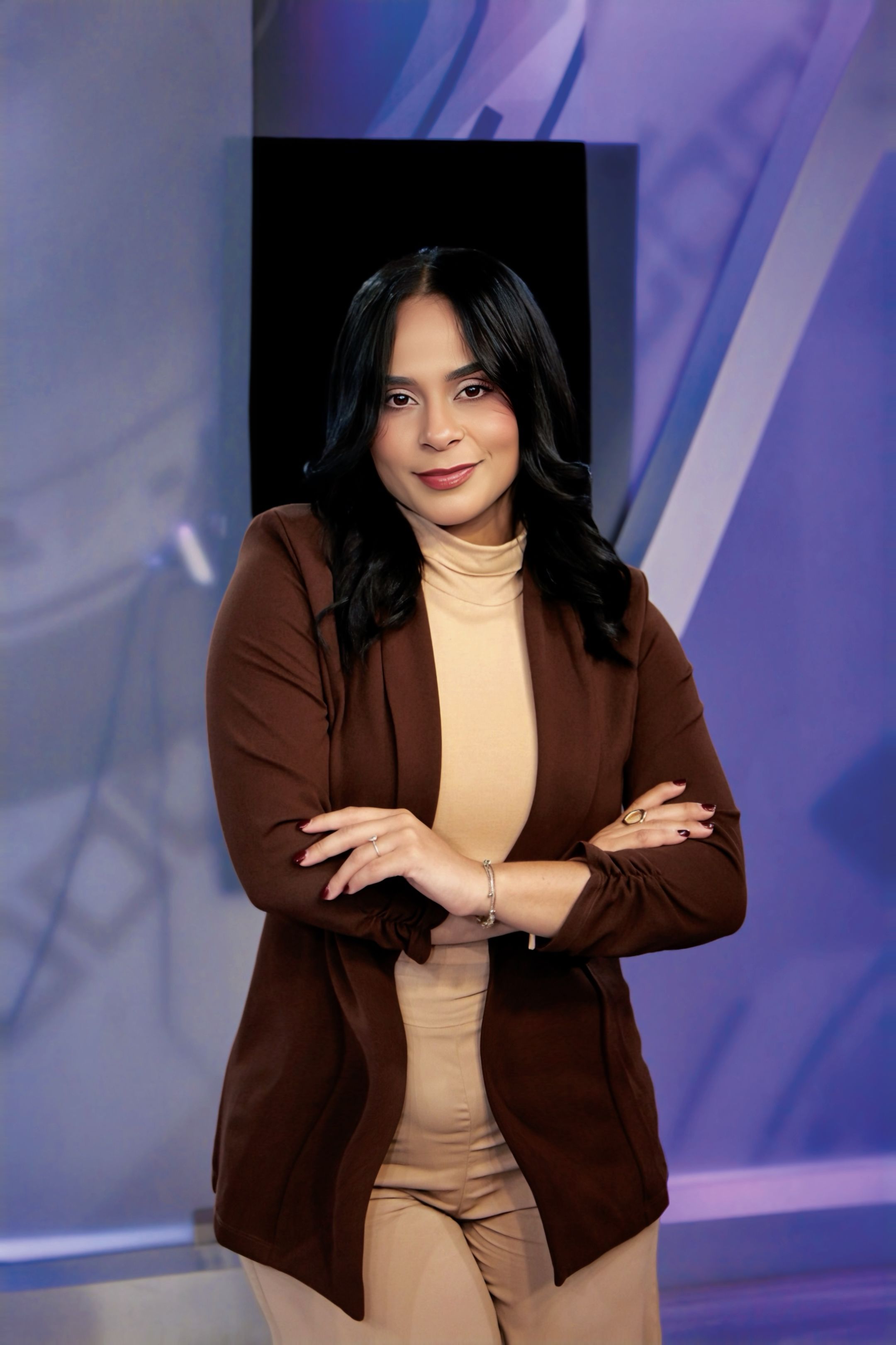 Confident woman standing in modern office with arms crossed, conveying professionalism.