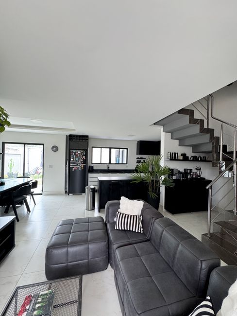 Fotomural Interior moderno y elegante con sofá negro, cocina y escalera en un espacio de estar bien iluminado.