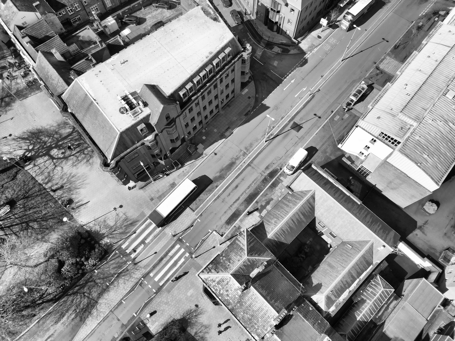 Monochrome aerial view of a city street with buildings, vehicles, and crosswalks.