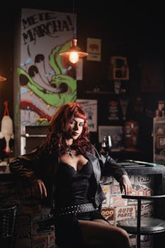 Stylish woman with red hair in a leather outfit, sitting in a vintage bar with graffiti art.