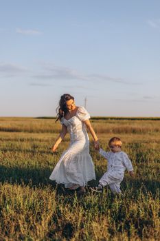A mother and her young child walk hand in hand through a sunny field, capturing a warm and joyful moment.