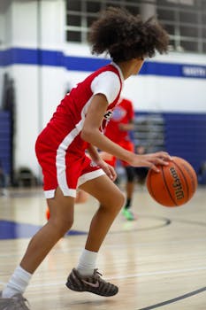 Young teenager dribbling basketball indoors wearing red jersey, focused on movement.