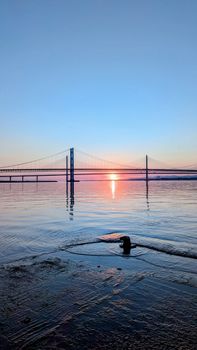Tranquil sunrise view over a suspension bridge reflecting on calm waters.