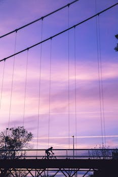 黄昏时分，天空浅紫，有人骑着自行车经过吊桥