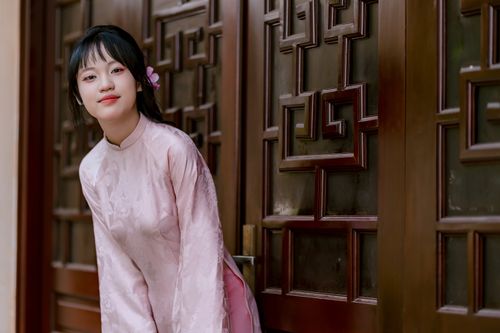 Free Portrait of a smiling young woman in pink traditional attire leaning against a decorative wooden door. Stock Photo