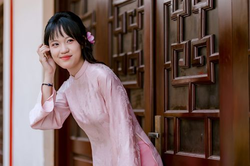 Free Portrait of a woman in a pink traditional dress, smiling by a wooden door. Stock Photo