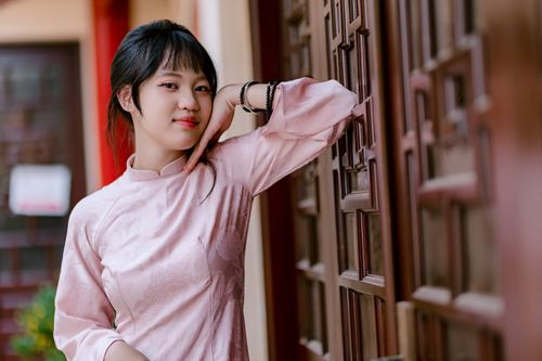 Free Portrait of a young woman in a pink traditional dress leaning against a decorative wooden doorway, showcasing elegance and style. Stock Photo
