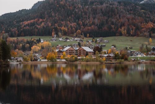 Free Scenic autumn view of a mountain village reflected in a calm lake, perfect for a peaceful nature getaway. Stock Photo