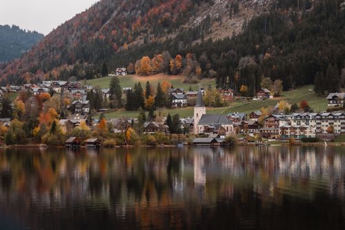 Free Picturesque village by a lake with colorful autumn foliage and mountain backdrop. Stock Photo