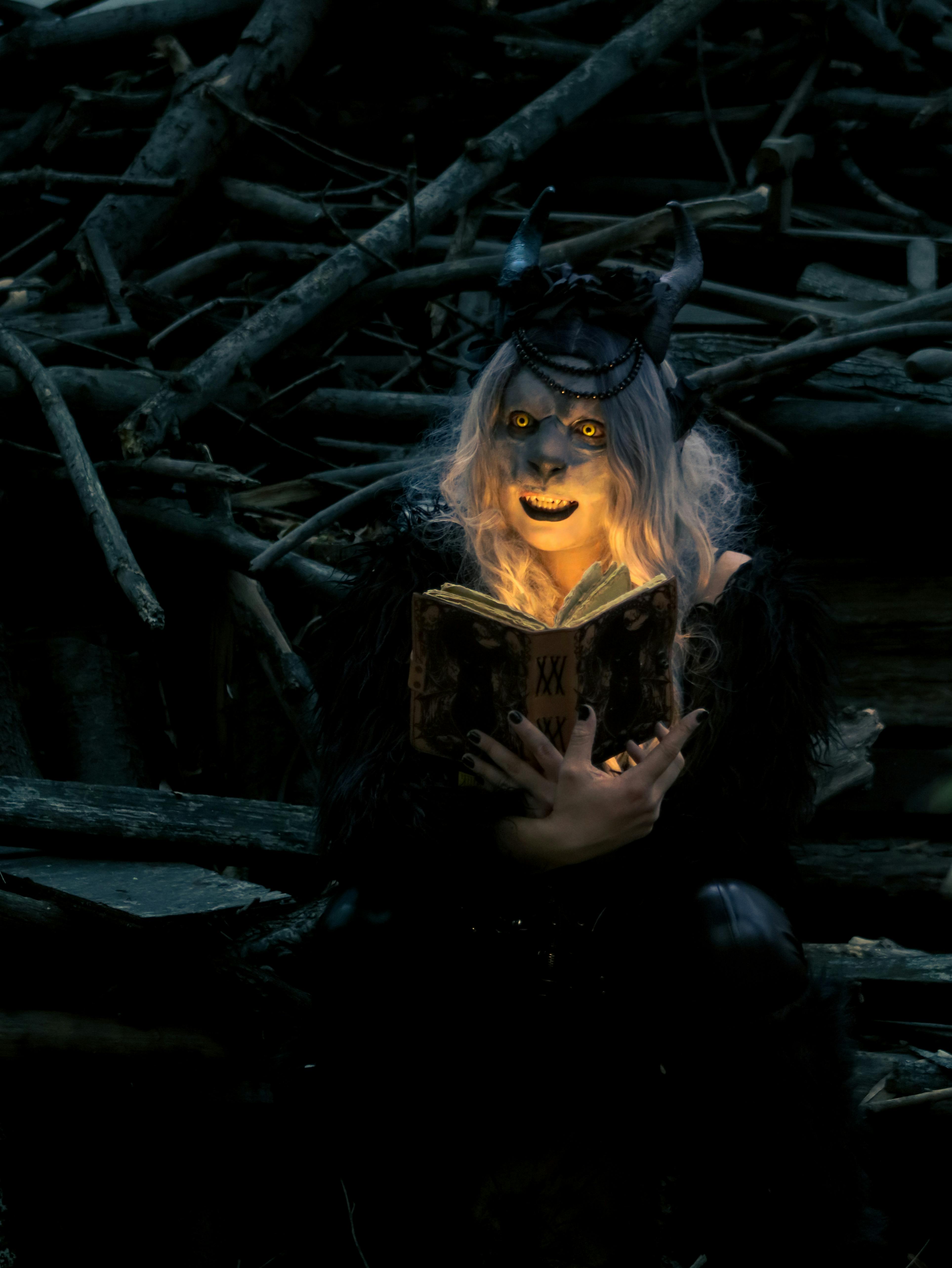 ingyenes Hátborzongató, misztikus alak, szarvakkal, melyeket egy könyv világít meg sötét erdei környezetben, titokzatos hangulatot teremtve. Stockfotó