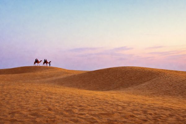 Two camels and riders crossing the Jaisalmer dunes at sunset