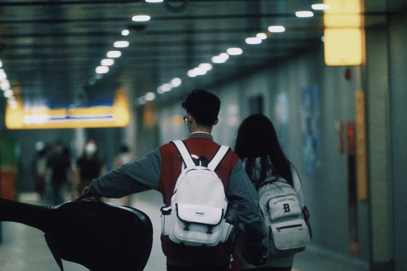 Two young travelers walking in a subway tunnel with backpacks, heading towards bright signage.