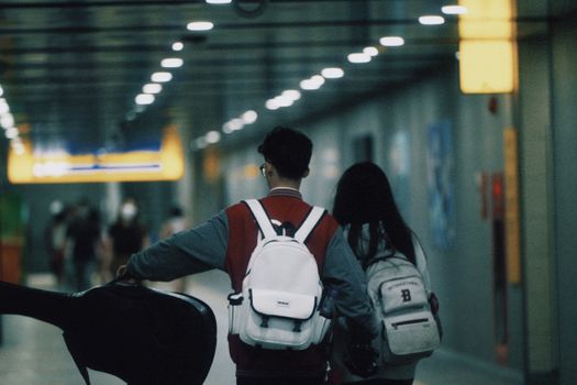 Two young travelers walking in a subway tunnel with backpacks, heading towards bright signage.