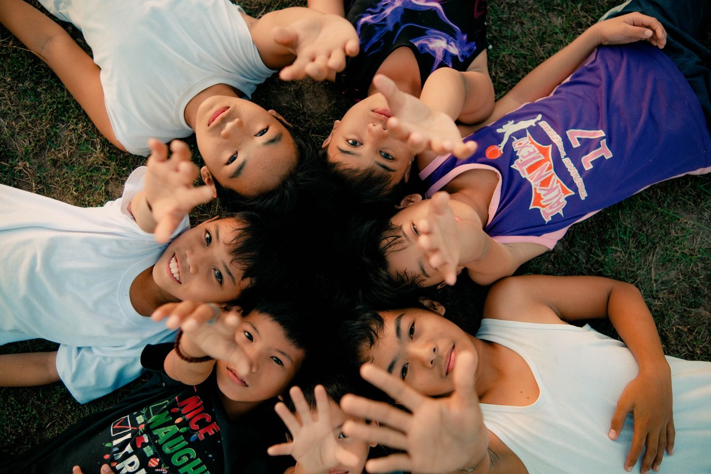 Joyful Filipino children lying on the grass, smiling and reaching toward the camera