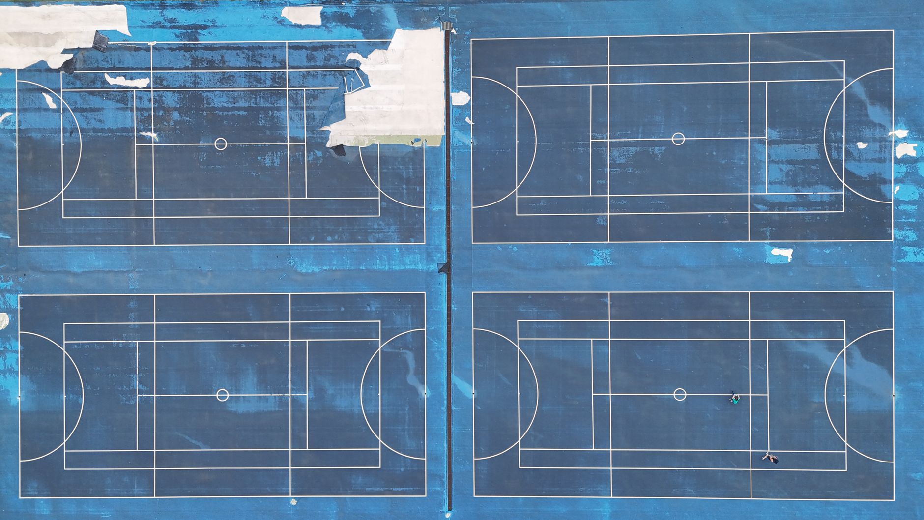 Drone shot of blue multi-sport courts with visible lines and wear from above.