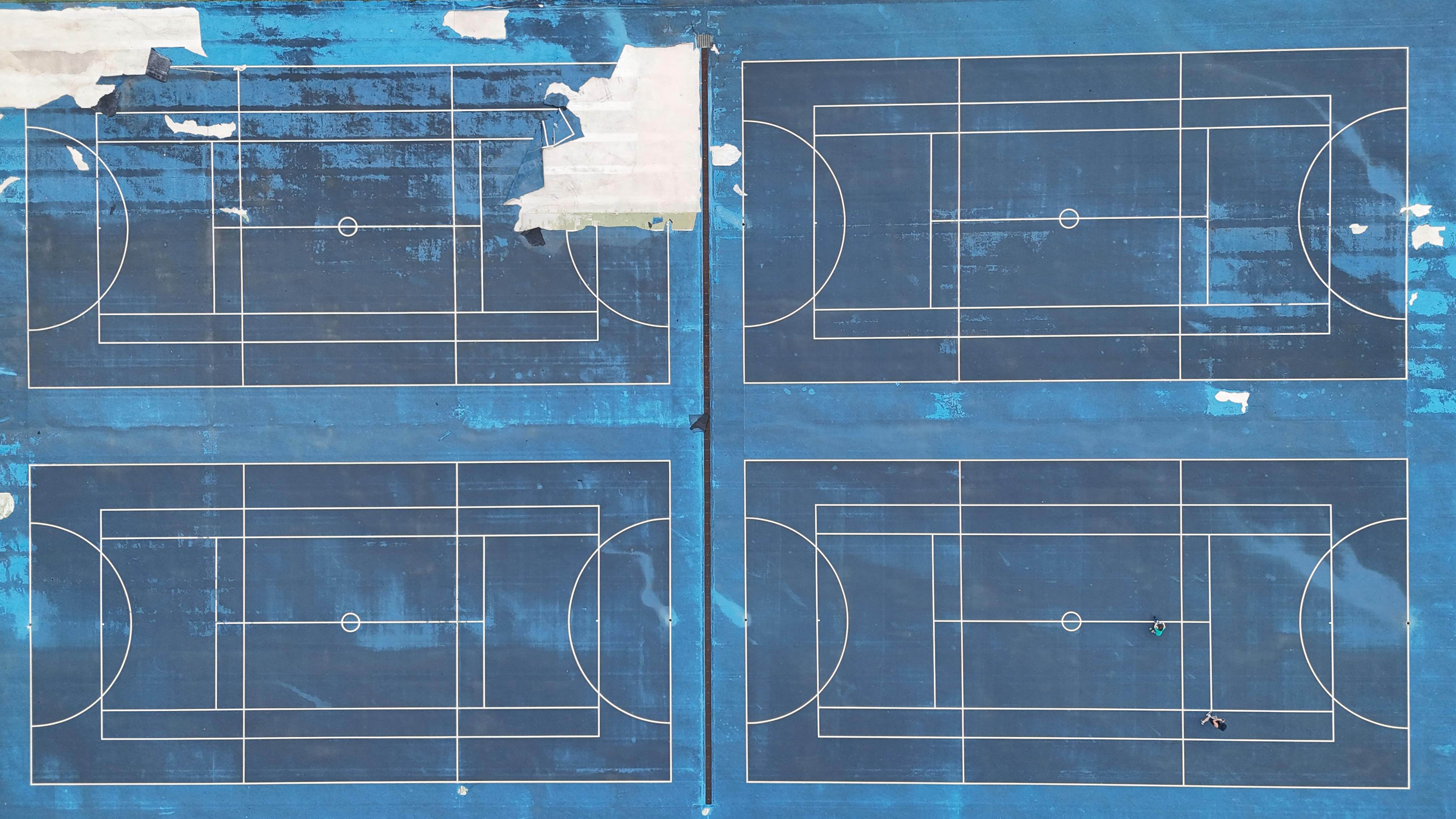 bezplatná Snímek dronem modrých multifunkčních sportovních kurtů s viditelnými liniemi a opotřebením shora. Základová fotografie