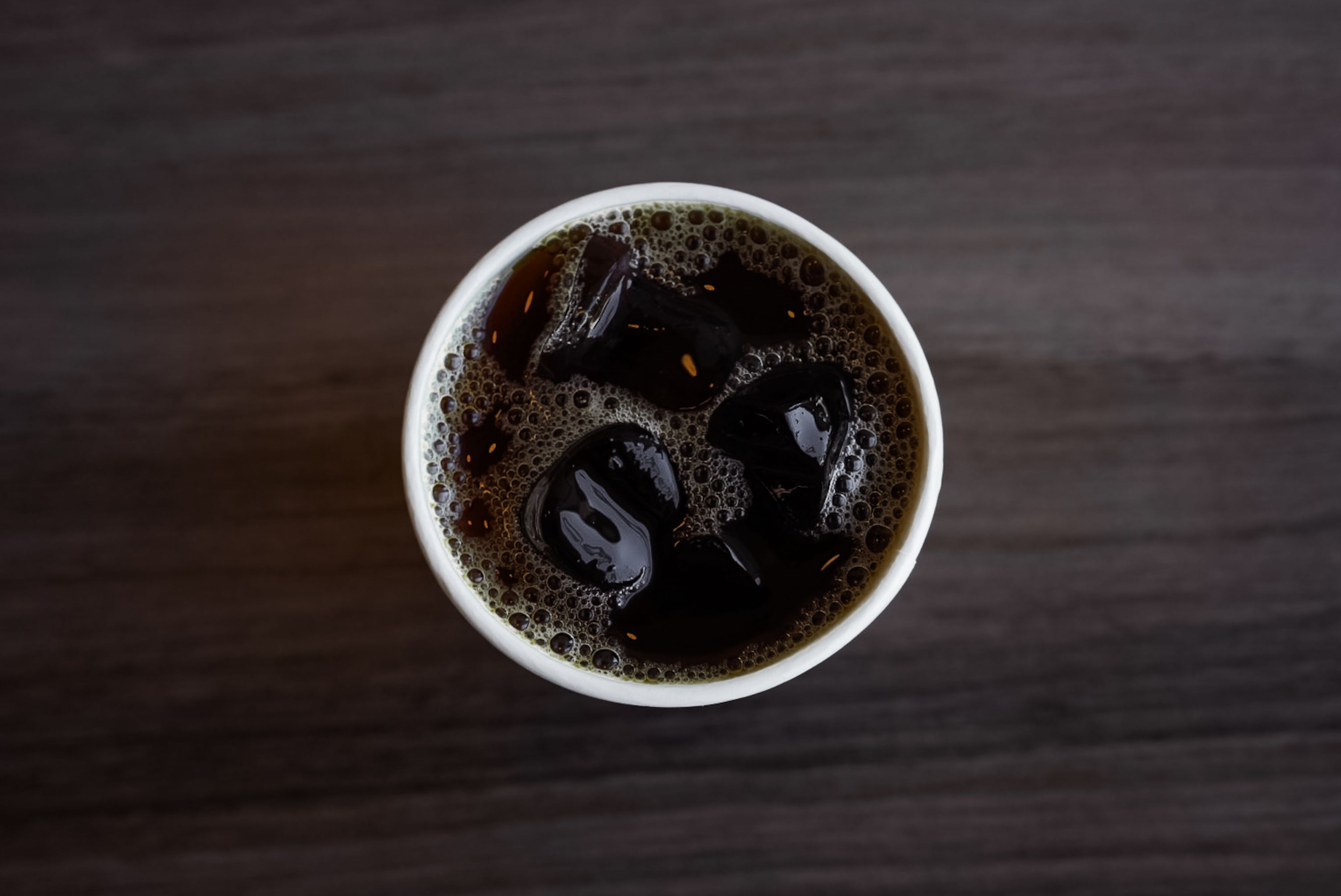 Aerial shot of a refreshing iced coffee in a cup on a wooden surface.